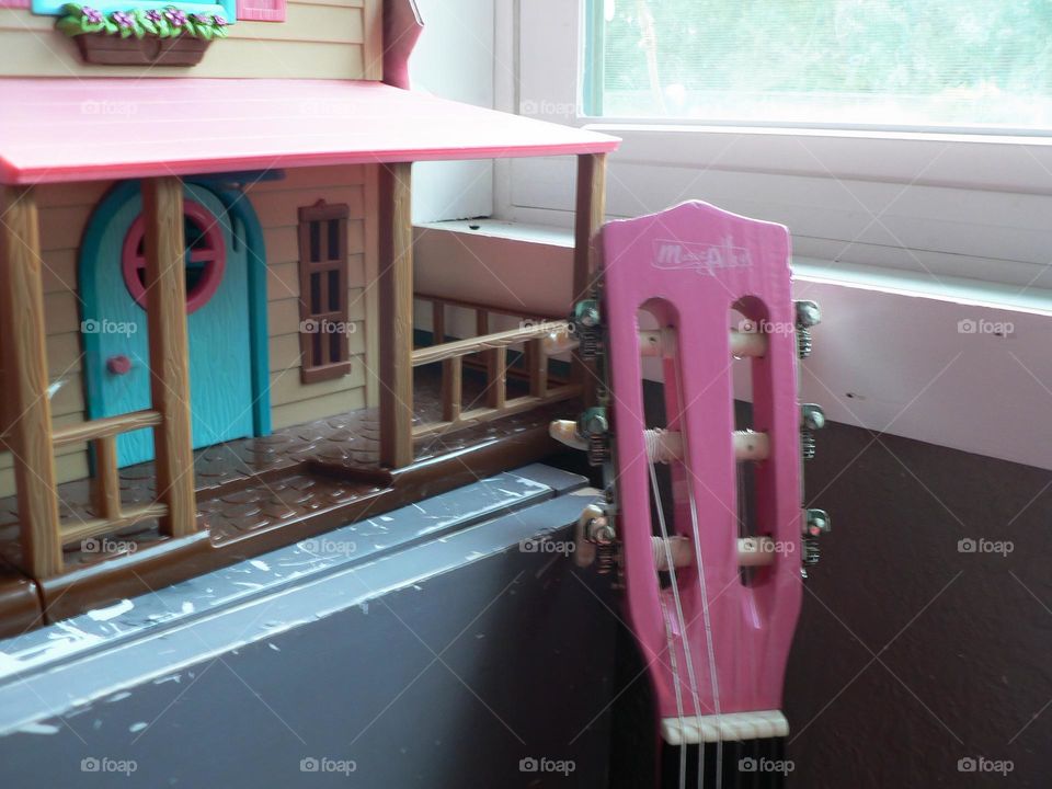 House play set with pink guitar against a blue violet grey dresser and window frame in the children bedroom close-up.