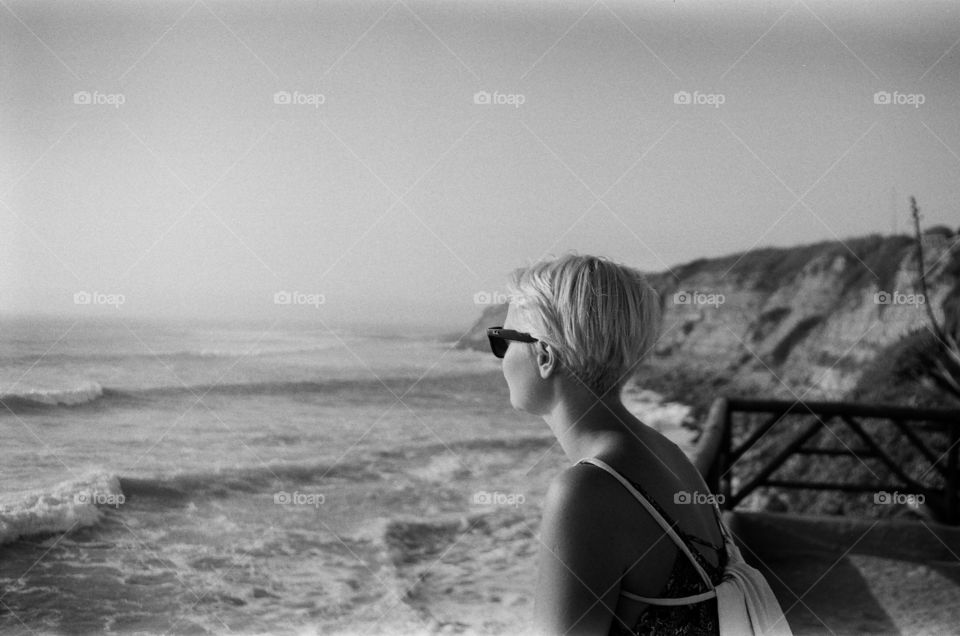 A young short-hair blond lady is thinking and dreaming looking at the Ocean 