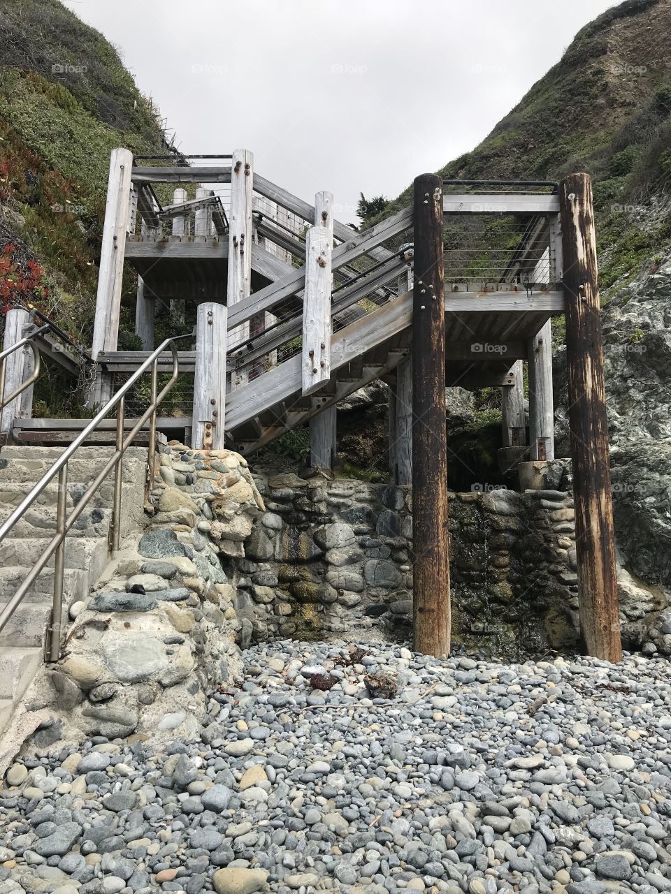 A weathered and criss crossing staircase leading from the beach back up to the winding road of highway 1. 