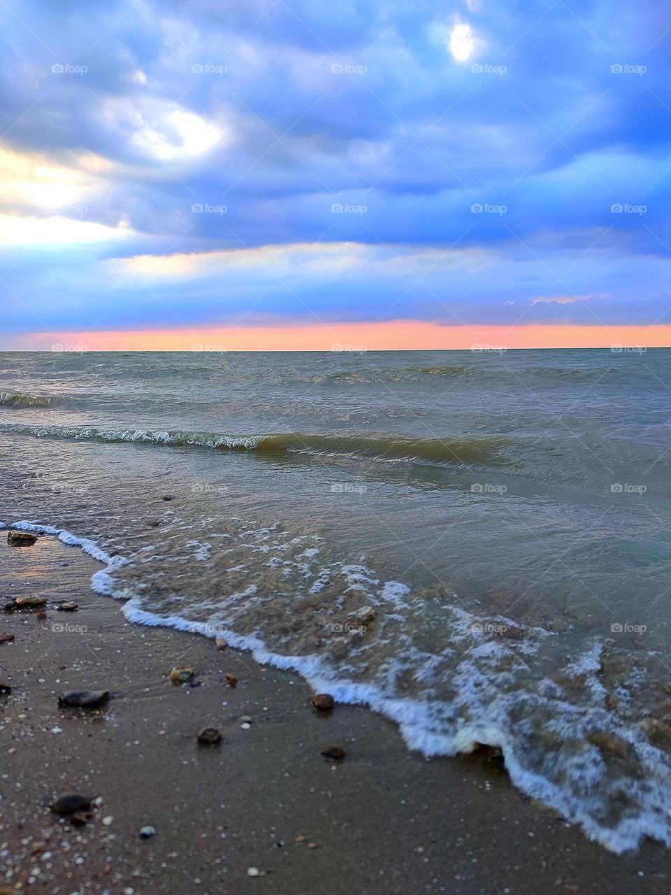 Sunset on the sea. The movement of the waves of the sea. The red stripe of sunset separates the stormy sea from the dark clouds of the sky