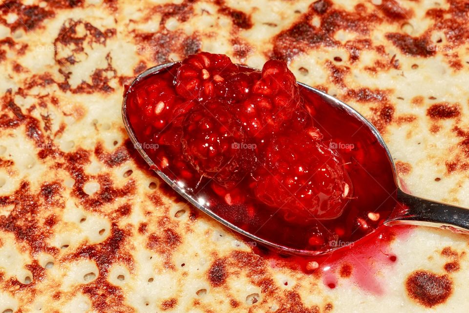Macro of spoonful full with raspberry jam in a pancake