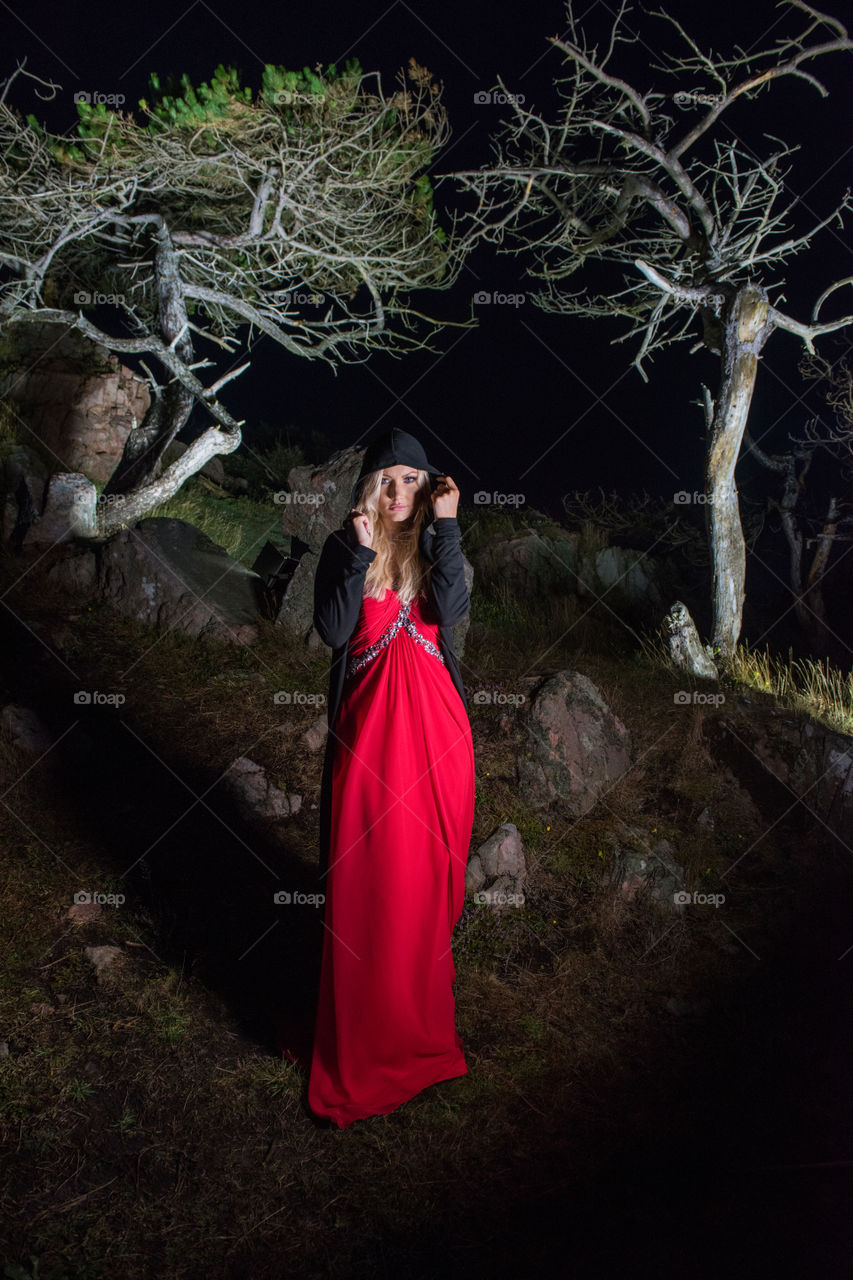 Woman in red dress wearing hooded jacket standing at forest