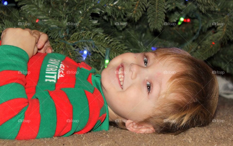 A little boy lying and smiling in front of christmas tree