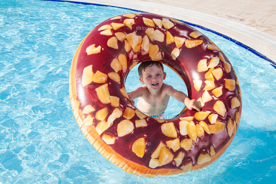 Little boy enjoying playing with inflatable doughnut ring in a swimming pool.