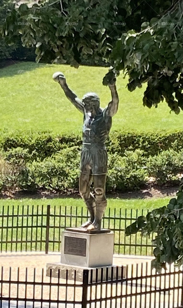 A statue that is a replica of Rocky Balboa with his boxing gloves on and his arms raised surrounded by a black iron fence