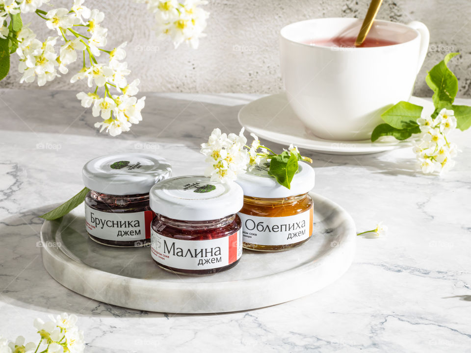 Different sorts of Marmeladeglases and white cup of tea and flowers in the background 