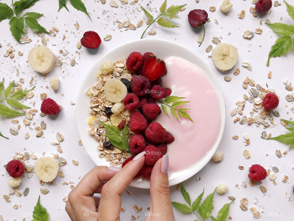 Female hand taking a red ripe raspberry from a plate with yogurt and muesli 