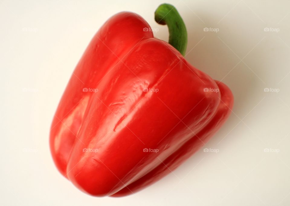 Red bell pepper with green stem on white background.