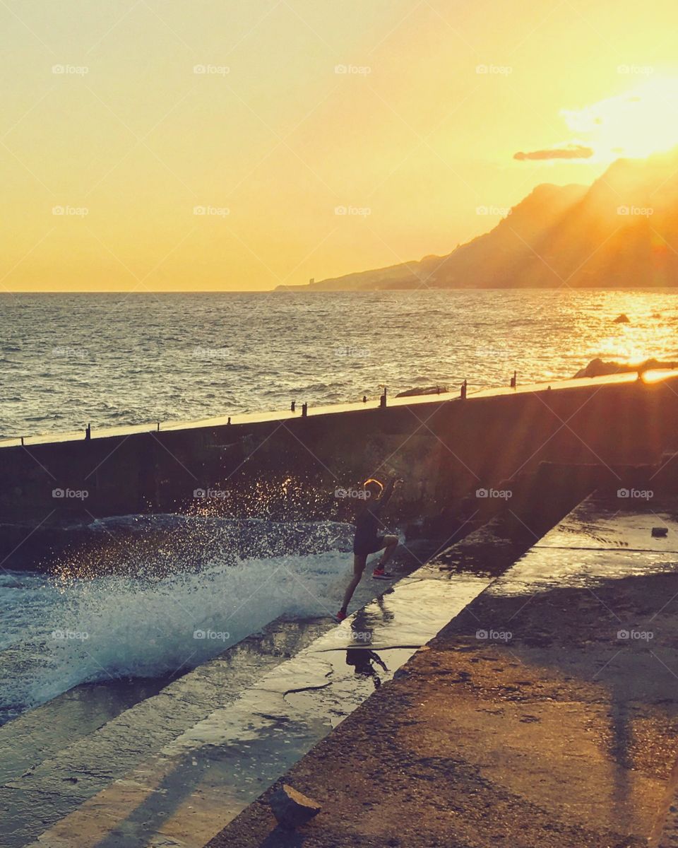 Boy playing with waves on the sea at sunset 