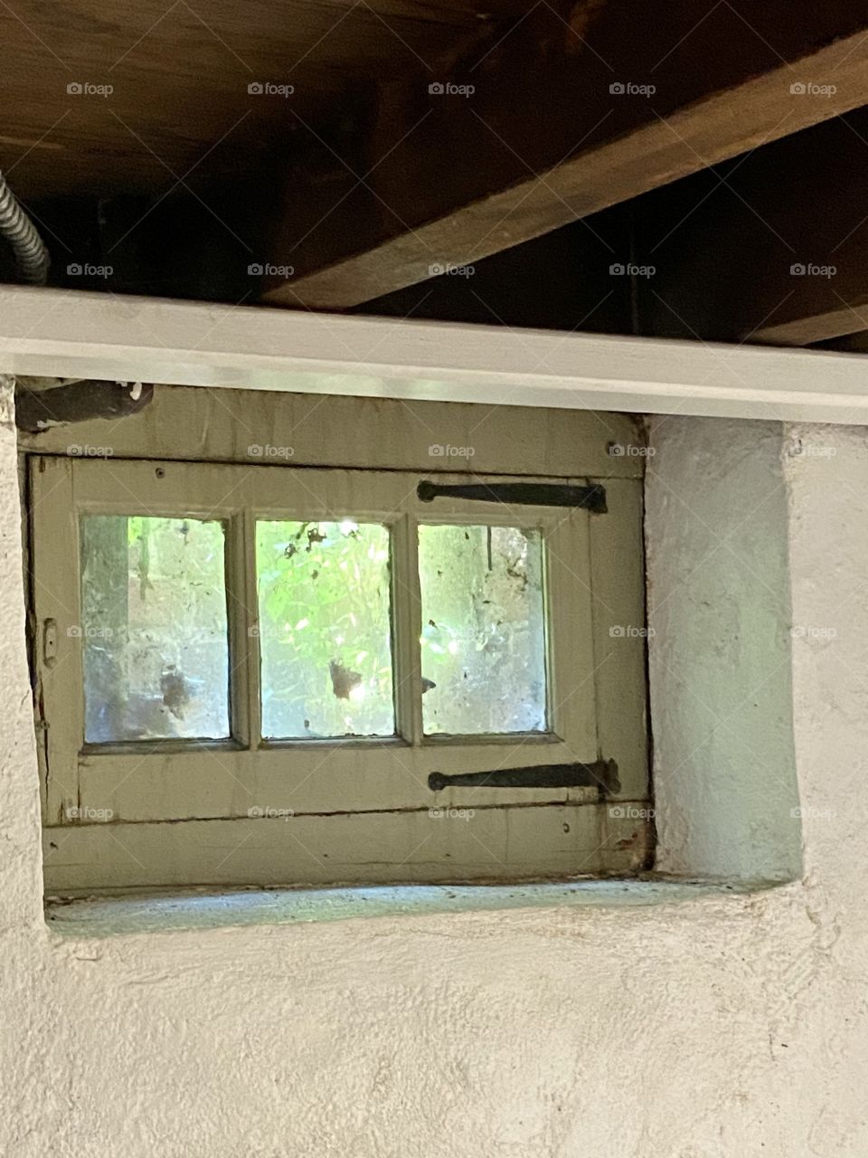 A small antique wooden window with three panes hanging in a concrete alcove in a basement