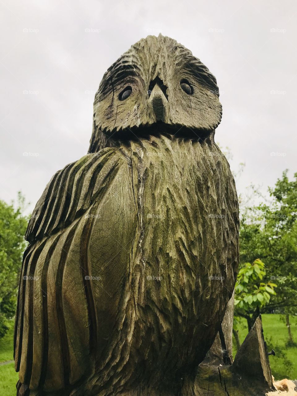 A wooden owl sculpture in an orchard