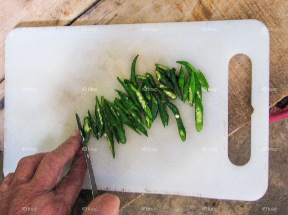 Close-up of a person cutting green chilies on a white cutting board in high angle view