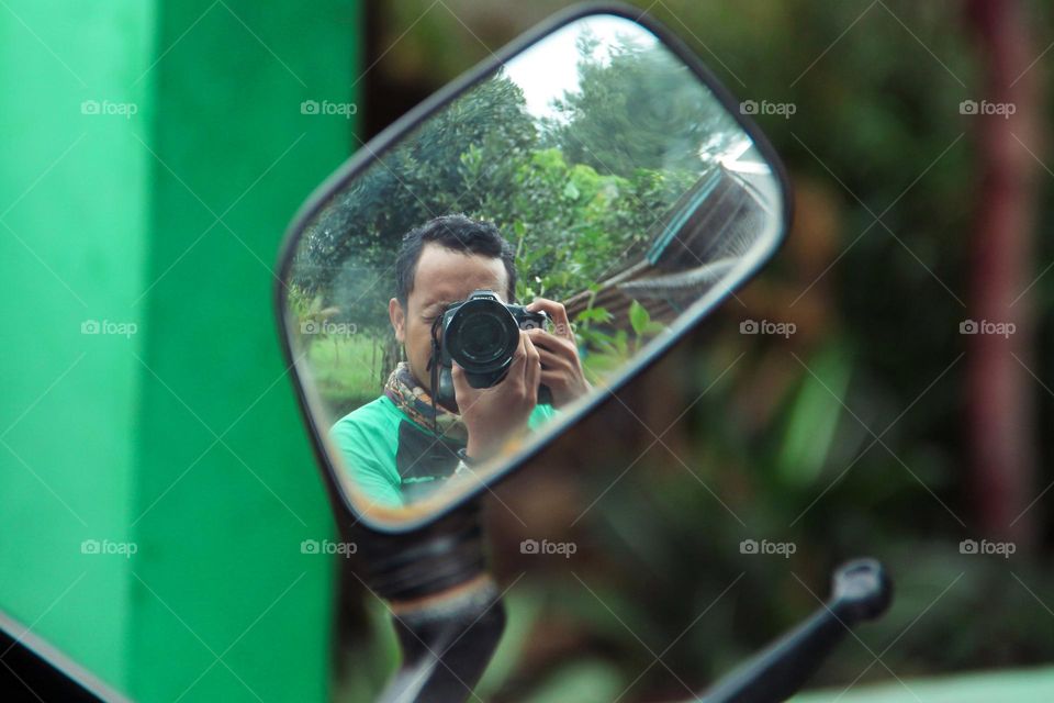 Selfie of an Asian man in the rearview mirror of a motorbike.