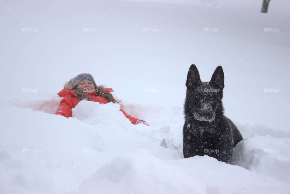 A young girl, and her German Shepard, playing in the snow. 