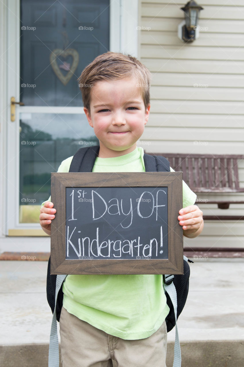 Young boy standing outdoors with a sign for his first day of kindergarten