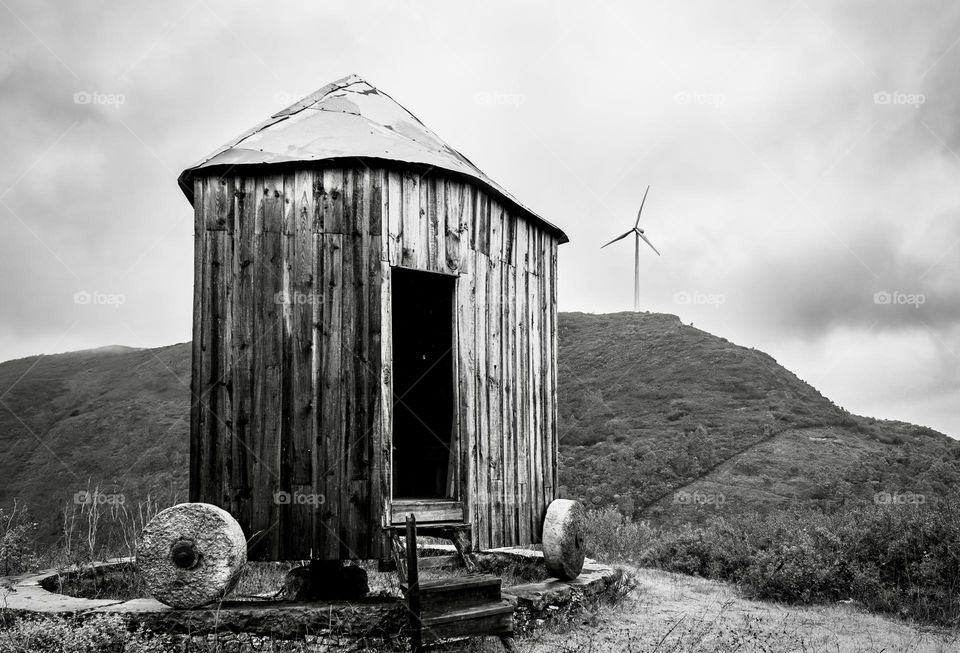 B&W landscape containing an old mill, with a new wind turbine in the background hill.