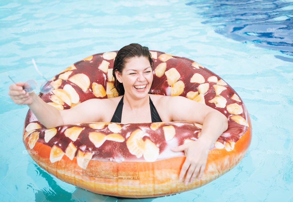 Happy young woman plus size body positive in inflatable doughnut circle swimming in the pool, summer vacations