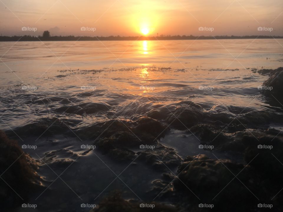 The sweeping water slushes over pebbles on an Island in the middle of the Indian River during sunset. 