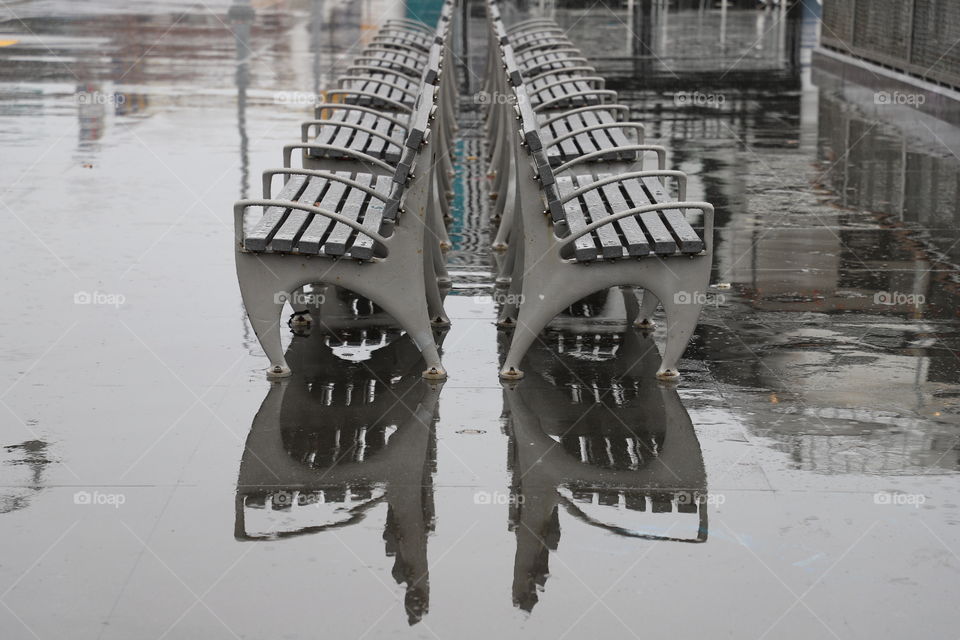 Row of benches reflecting on the wet ground