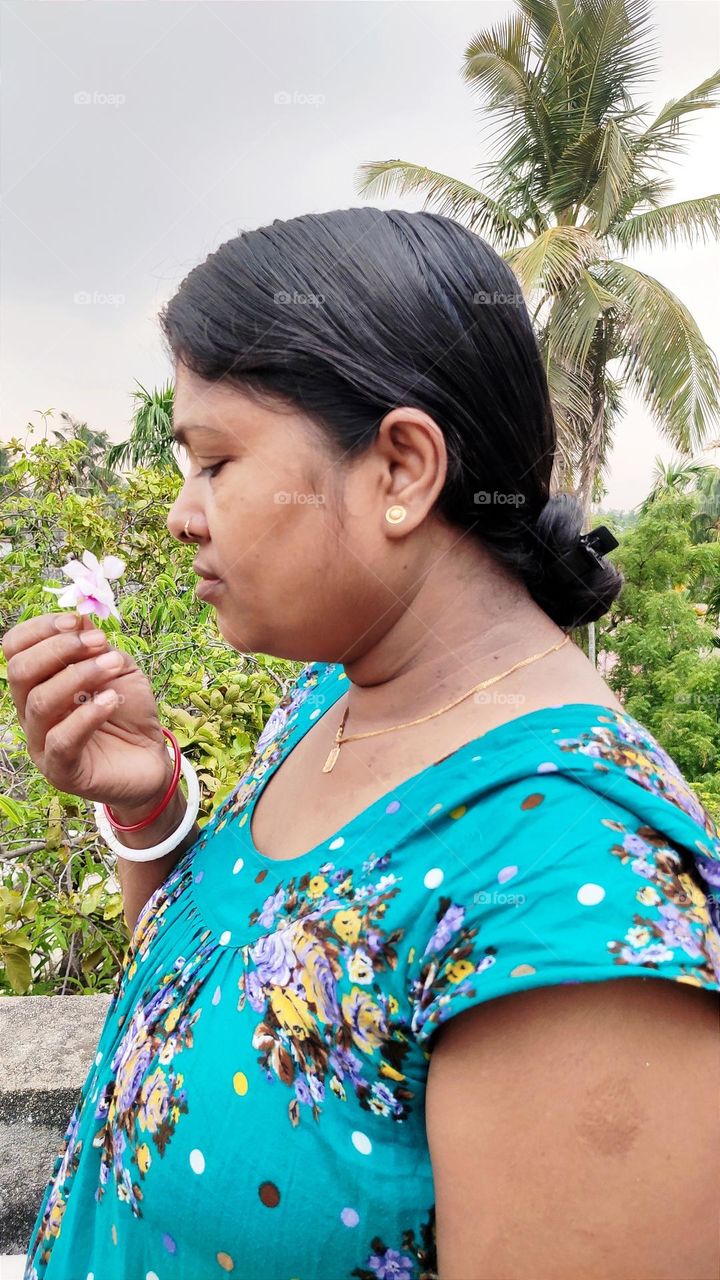 One lady is taking the smell of a flowers. She is enjoying the fragrance in her garden.