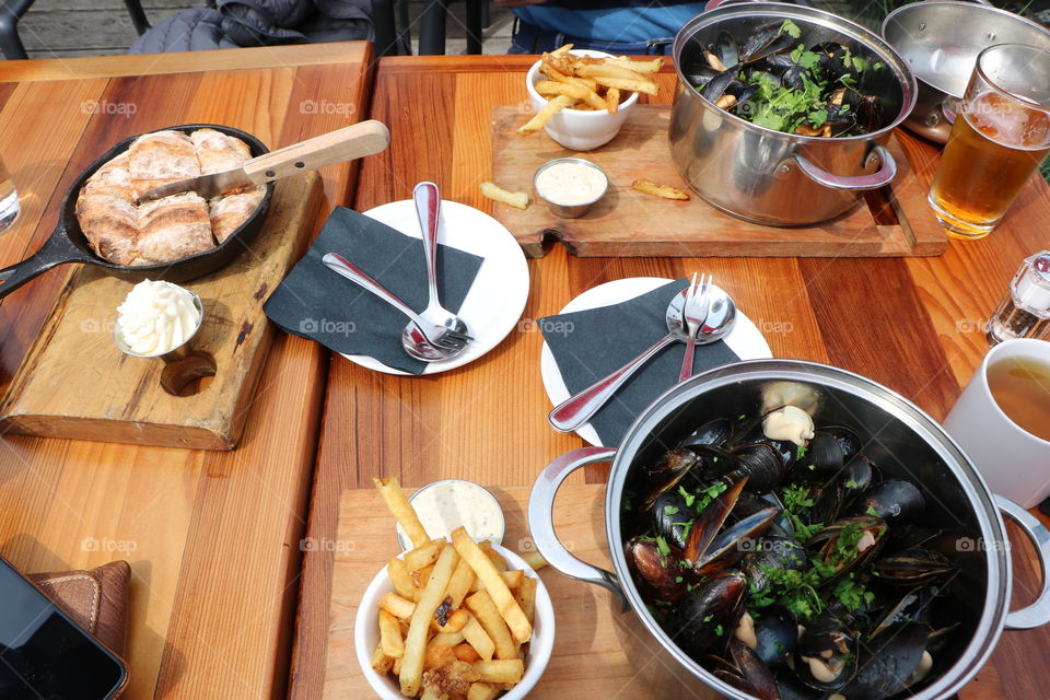 Let’s it seafood- mussels broiled in a pot , fries and home made bread on a nice table setting 