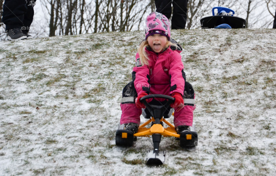 Young girl of five years old riding the sledge down a hill.