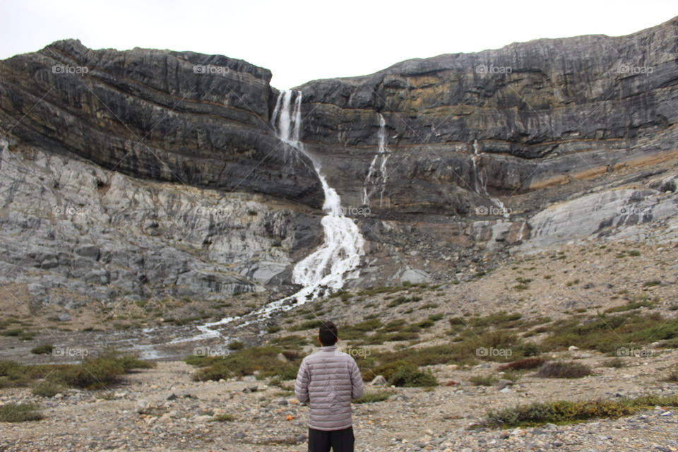 Guy standing next to a waterfall. 