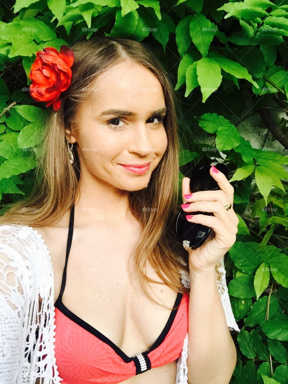 Selfie of woman with long dark blonde hair with black sunglasses in her hand standing against background made of leaves