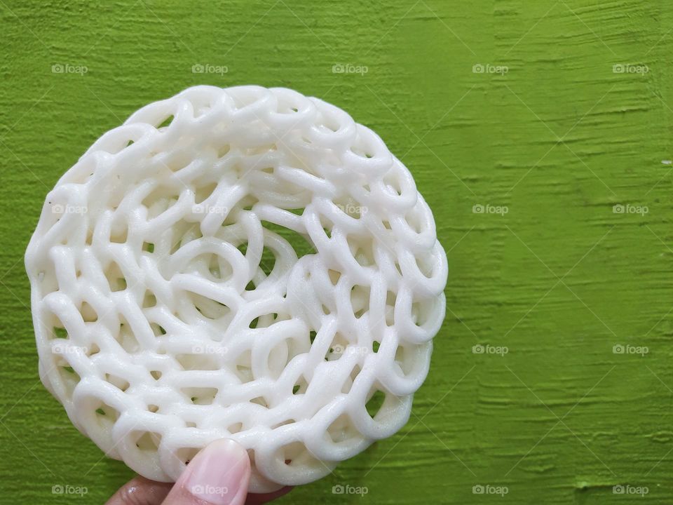 White crackers are Indonesian traditional fried crackers named kerupuk putih made from starch mixed with fish or spices, isolated on a green background