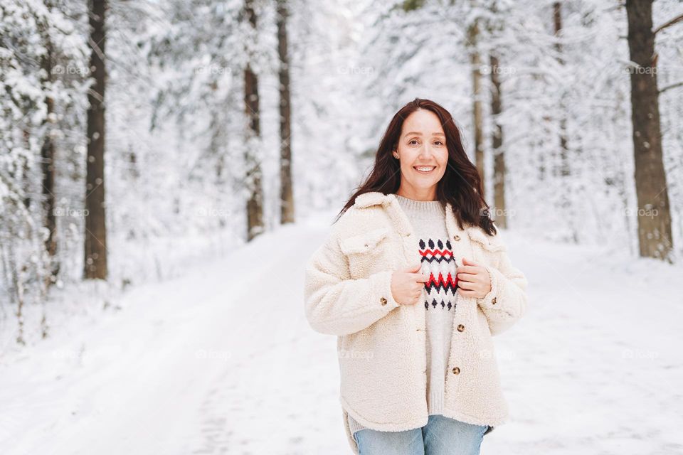 Smiling adult woman with dark hair in winter clothes in snowy winter forest