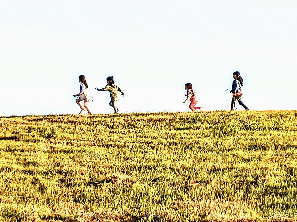 silhouette of four girls playing in the distance on a hill