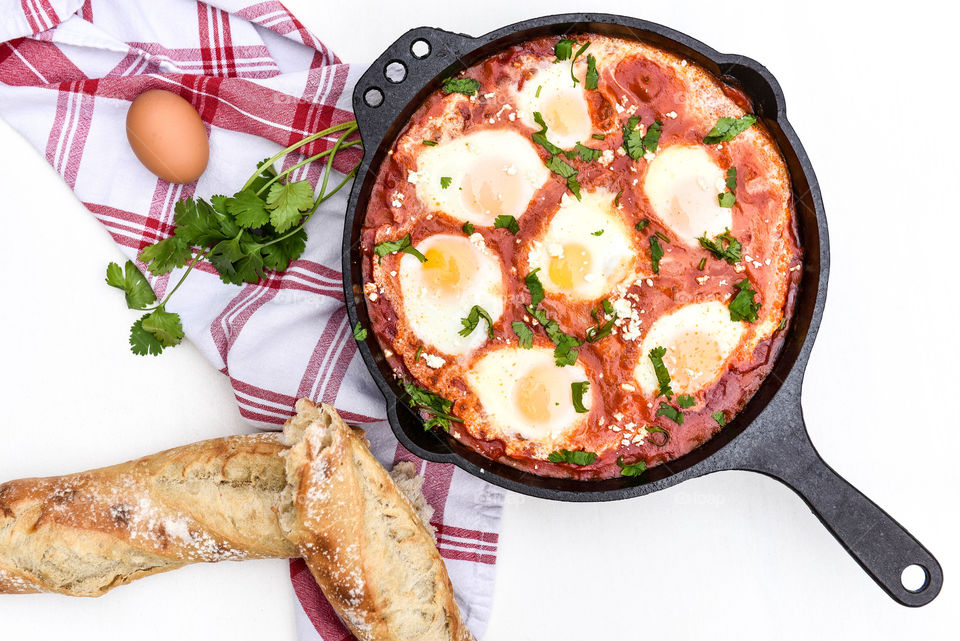 Top view flat lay of a shakshouka dish in a cast iron skillet surrounded by ingredients