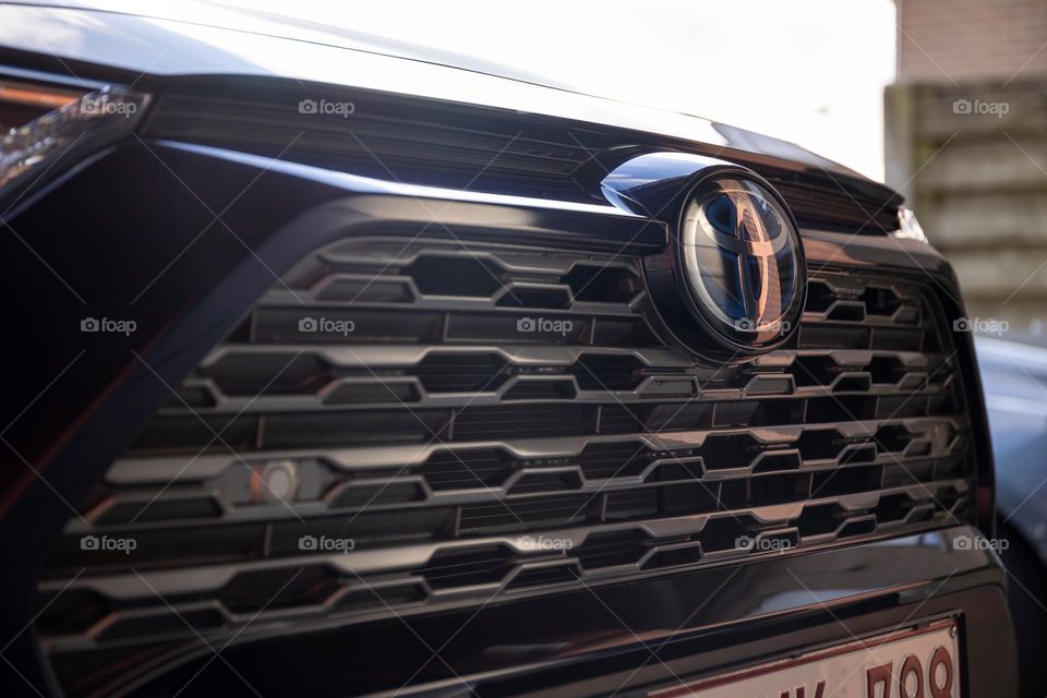 A portrait of the grill at the front of the car of a toyota. the emblem of the company is visible.