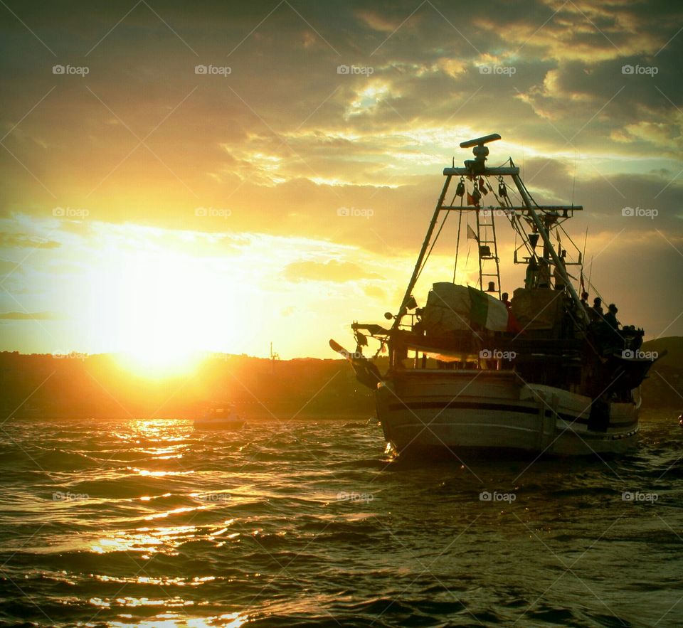 Fishing boat coming back to its harbor at sunset. Gaeta, Italy