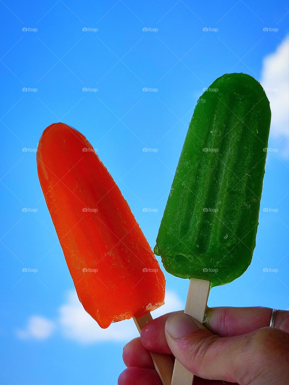 Color contrast: green and red. Hand holding green ice cream and red ice cream against blue sky