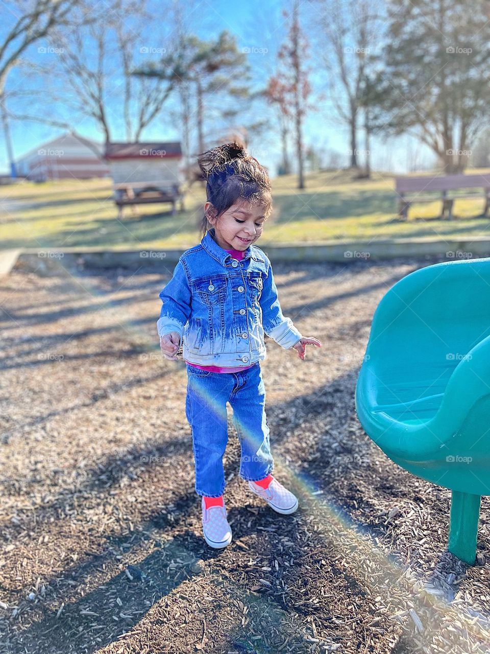 Toddler girl jumping in park, toddler wearing Jean jacket, toddler girl smiling in the park, outdoors is her happy place, being outside makes toddler happy, toddlers facial expression of happiness, showing happiness while playing outside