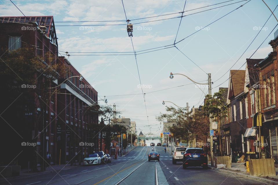 A busy street of cars, streetcar wires and people. Bridge in distance