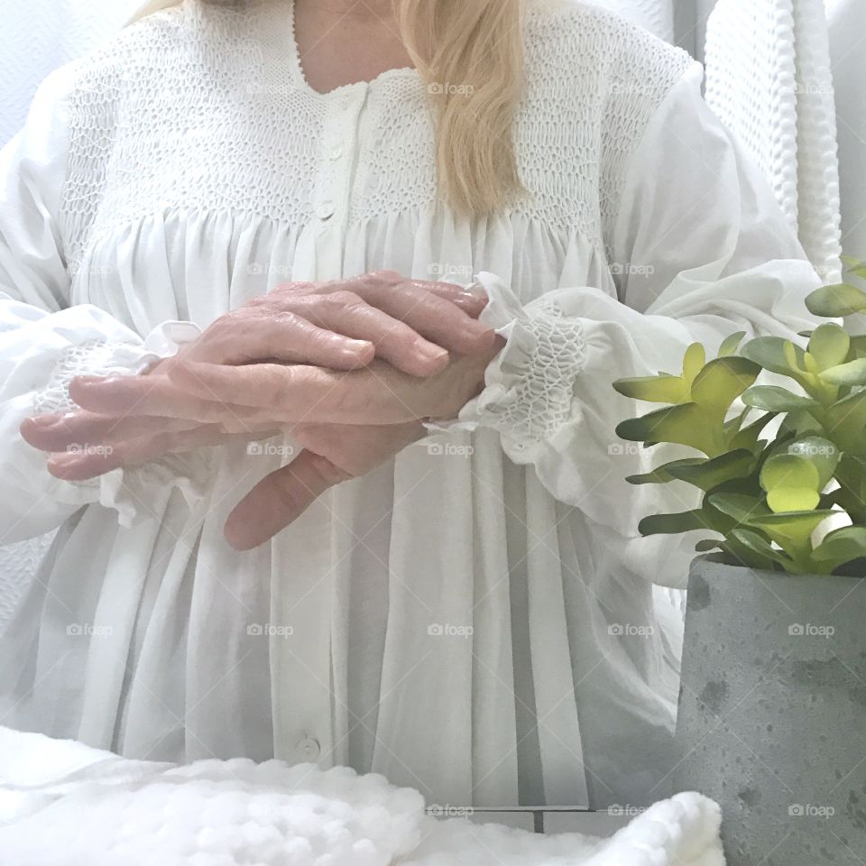 A woman applying lotion to her hands! Wearing white and standing in a white room!