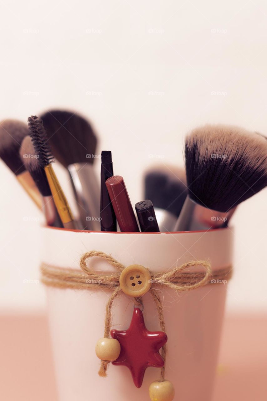 Set of makeup brushes and pencils for lips and eyes in a porcelain New Year's Eve bucket on white background, close-up view from below. Concept makeup items, beauty salon.