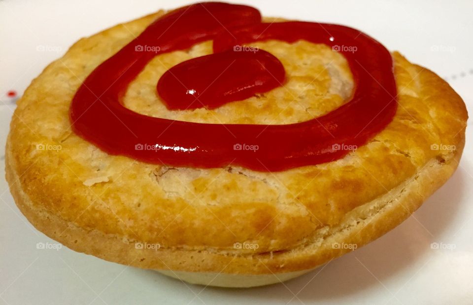 Meat pie. A pastry meat pie with tomato sauce swirled on top on a white plate
