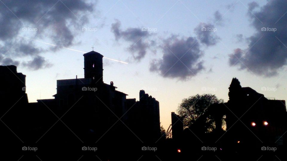silhouette of a church with airplane tra il in the clouds