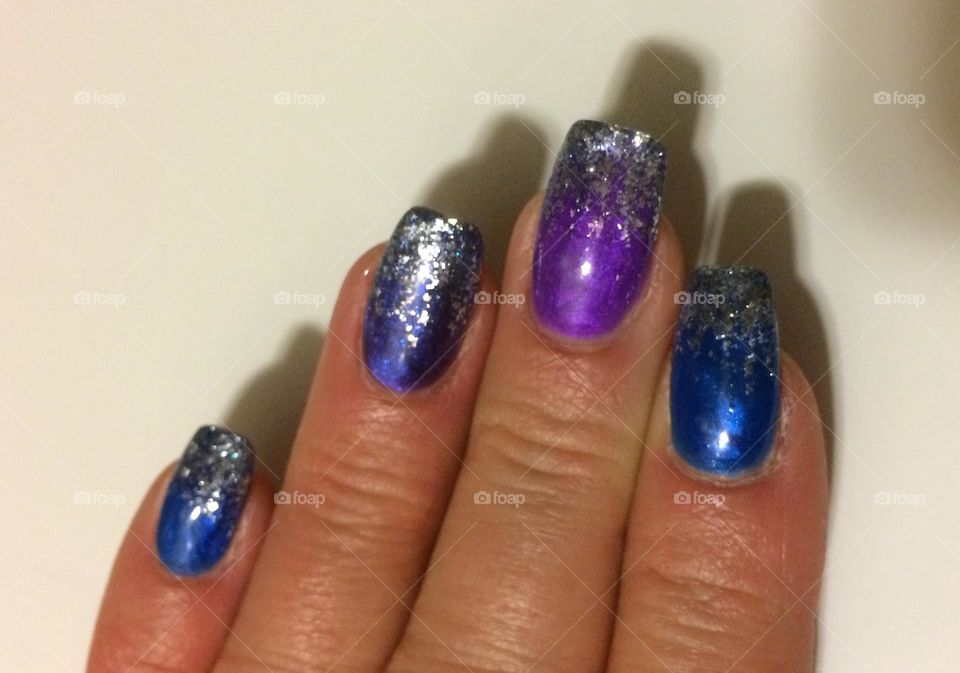Long Blue and purple, sparkly, silver glitter Manicured nails on a middle aged lady