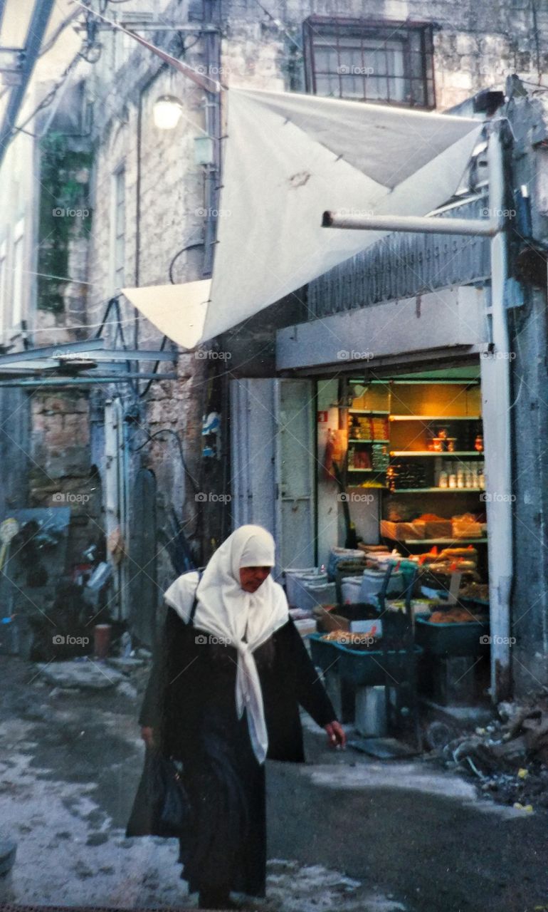 A women walking by the warm glow coming from a small shop in Nazareth, Israel.