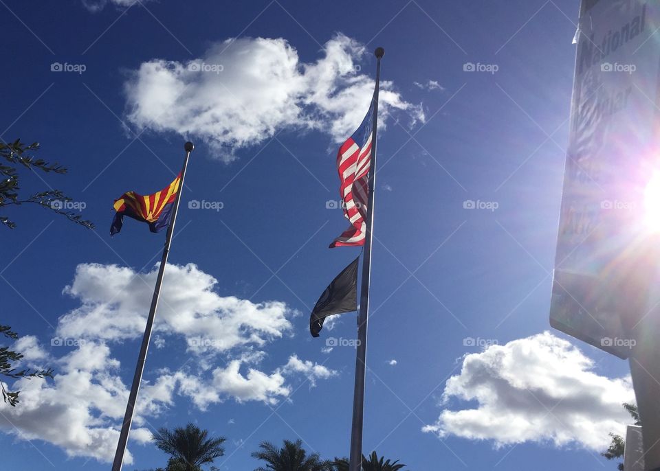 The State flag of Arizona and the American flag fly in front of the Arizona State Capitol.