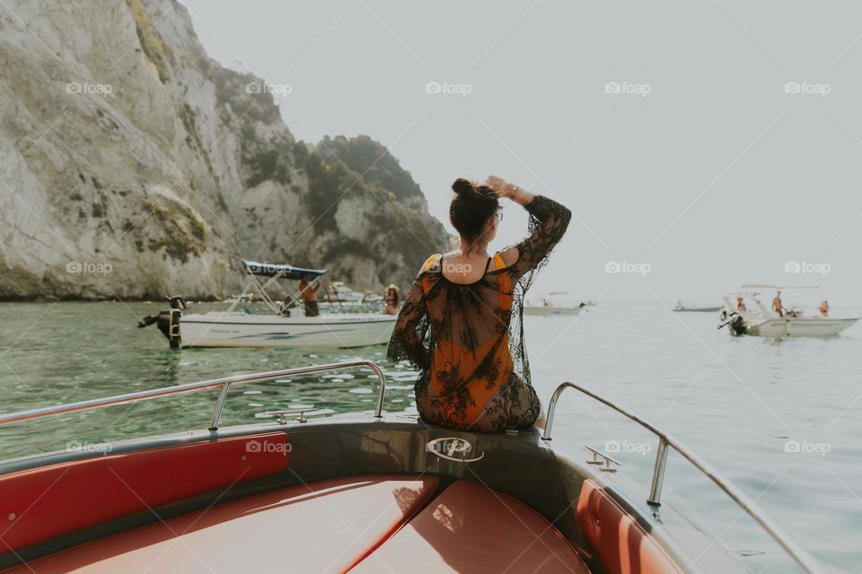 Portrait of one Caucasian young girl in a yellow swimsuit and a black openwork cape standing from the back on the edge of the boat and looking into the distance into the endless sea, close-up side view.