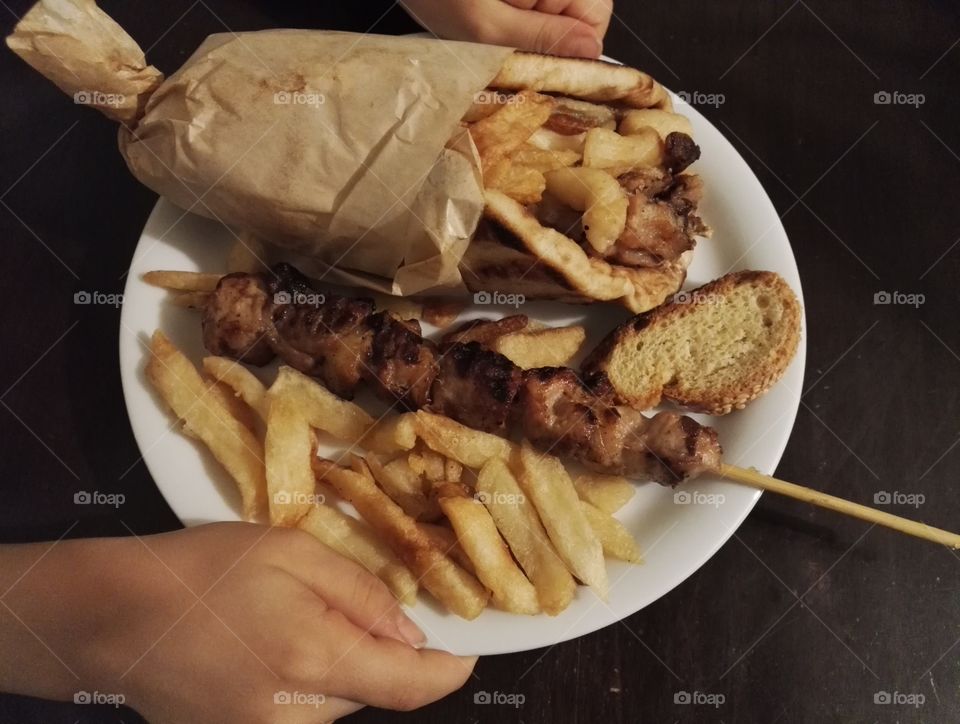 child's hands holding plate with pita gyros, meat stick and french fries