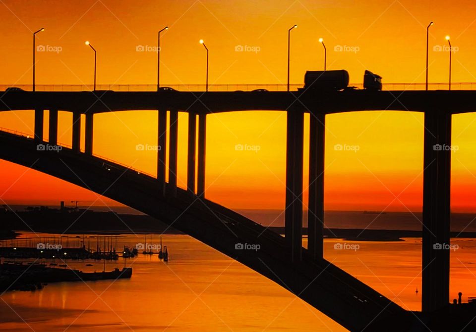 Drive time traffic crosses Ponte Da Arrábida at sunset in the river city of Porto