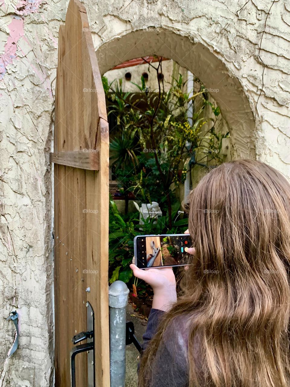 Spanish old style architecture residential large house built in the early 1900s. Backyard doorway with antique style, view on both side of the wall, young girl taking photos facing the tiled walkway sidewalk with trees in a beautiful tropical garden.