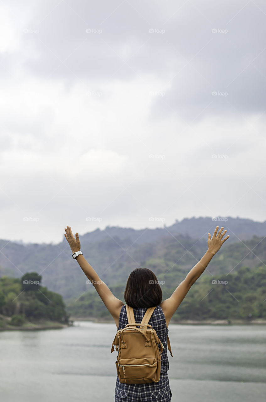 Women raise their arms and shoulder backpack Background mountains and water at Wang Bon dam ,Nakhon nayok in Thailand.