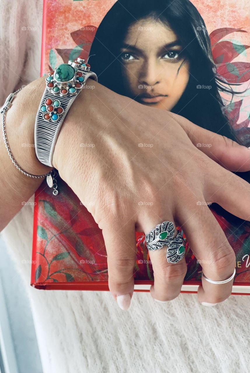 Woman’s hand wearing silver bracelets, silver rings and white nail polish holding a book 